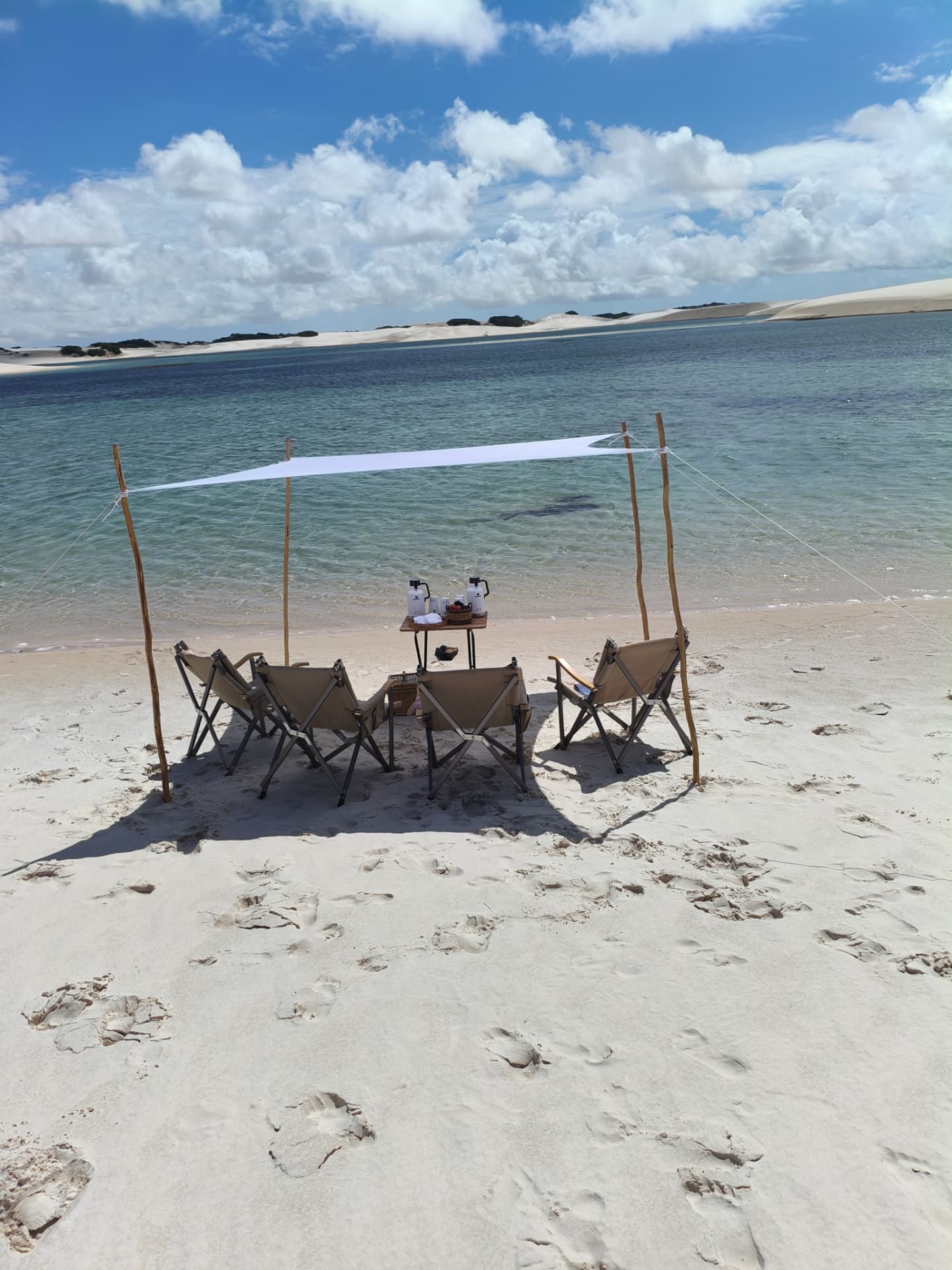 Cadeiras e tenda branca montadas na areia à beira da lagoa