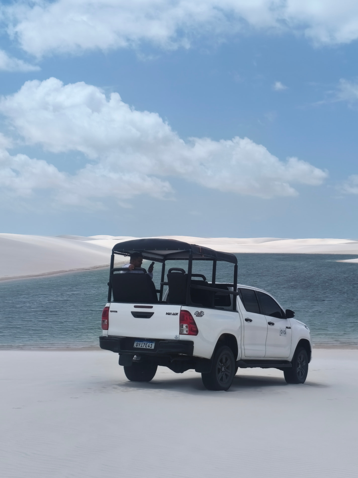 Toyota Hilux 4x4 branca sobre a areia branca diante de uma lagoa