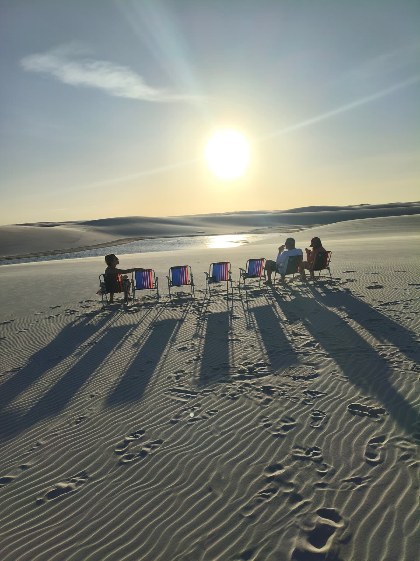 Grupo de visitantes sentados em cadeiras de praia sobre a duna assistindo ao pôr do sol